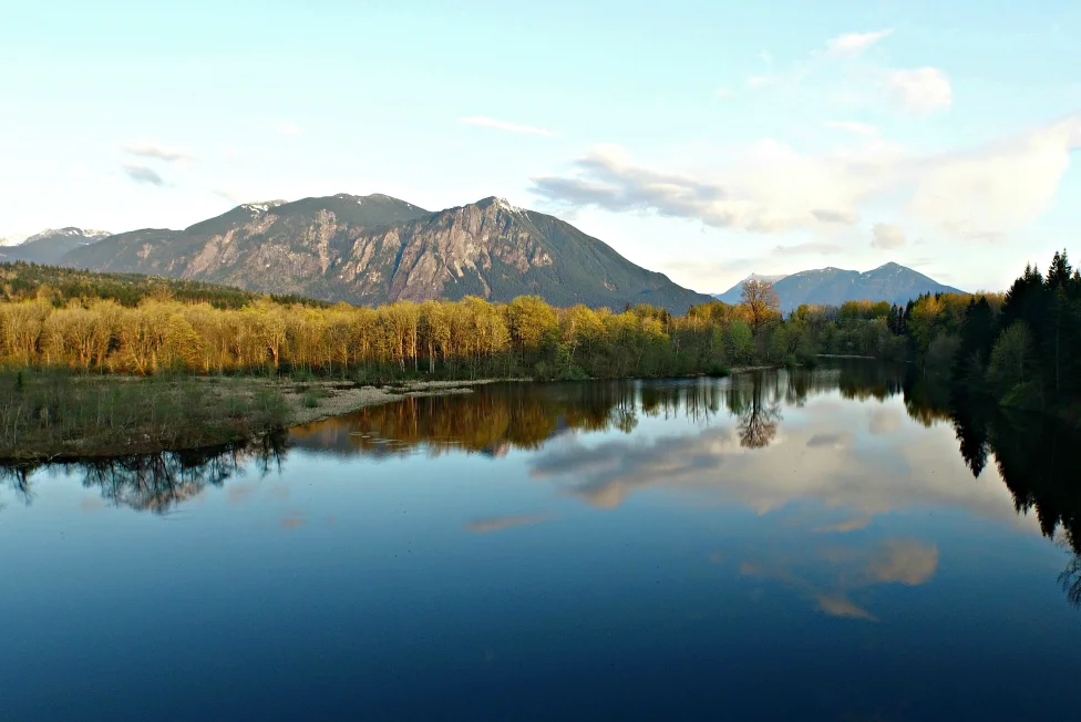 Mount Si reflected in a calm river with the Cascade foothills behind it